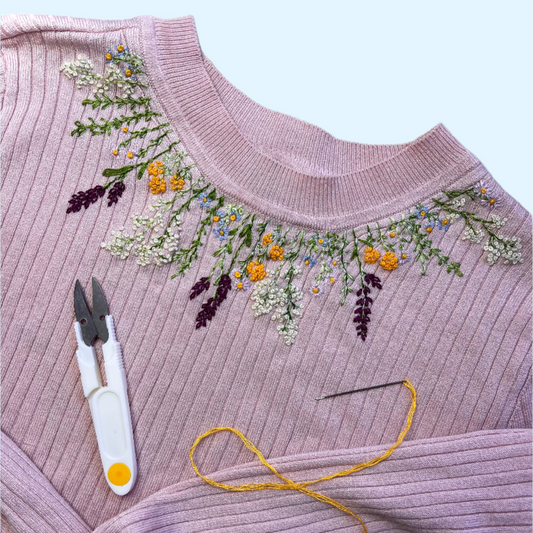 Pink sweater with floral embroidery, scissors, and thread on a white background
